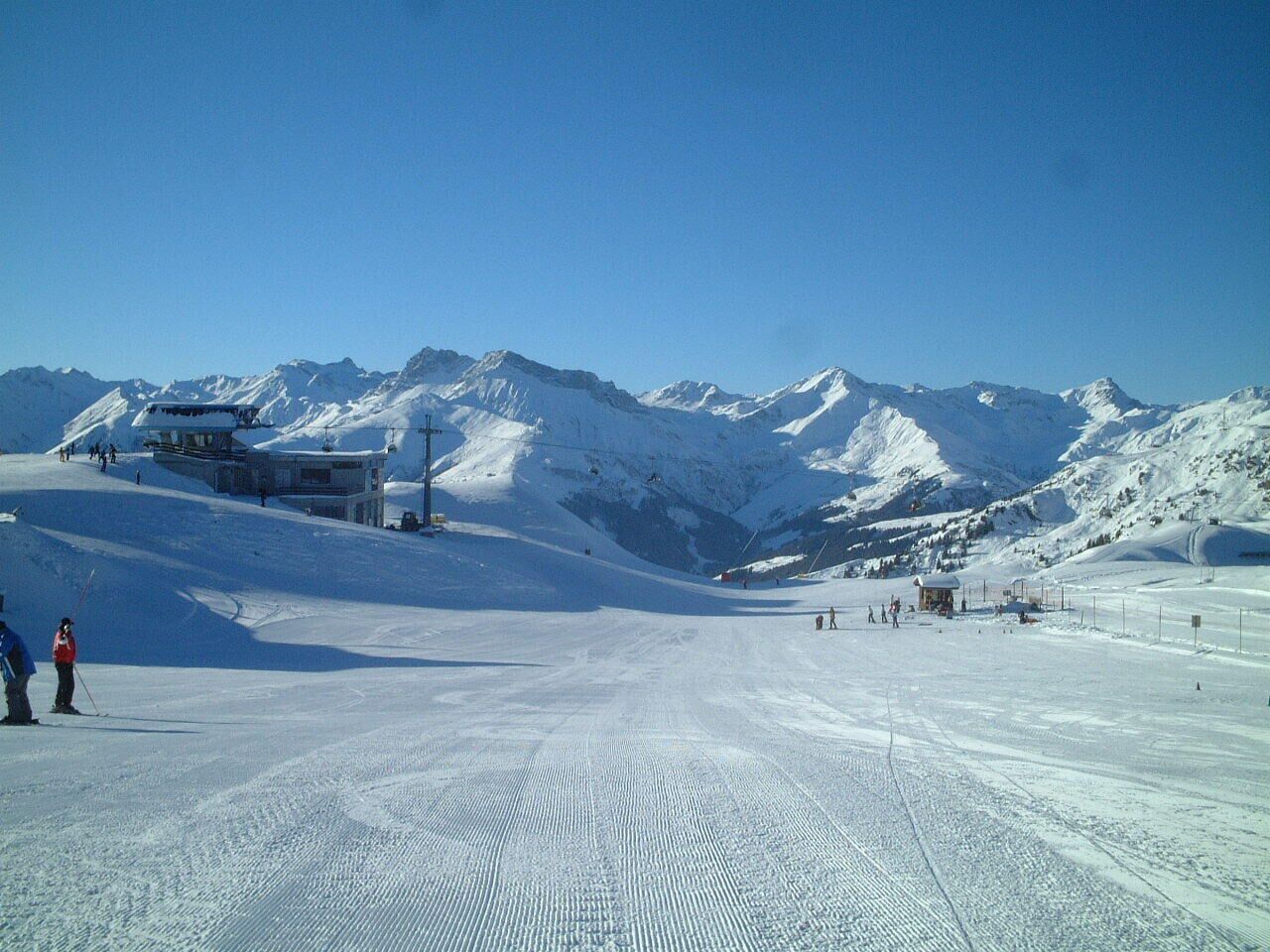A snow-covered ski slope with a chairlift, a small lodge, and distant mountains.