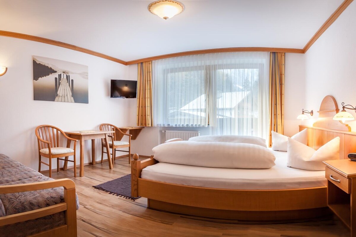 A hotel room with a bed, a desk, a chair, a television, and a window with curtains.
