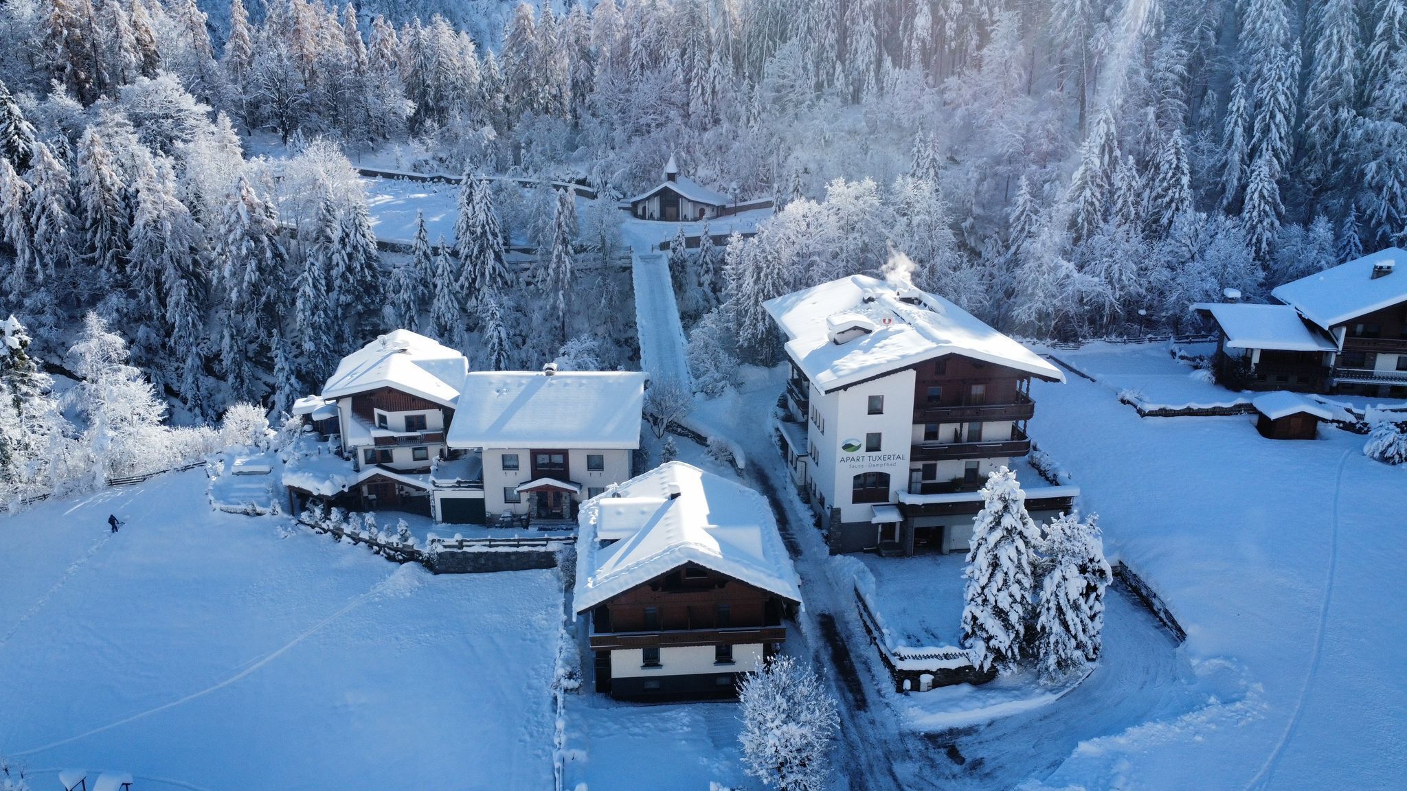 A snow-covered lodge with multiple buildings, a ski lift, and a forested backdrop.