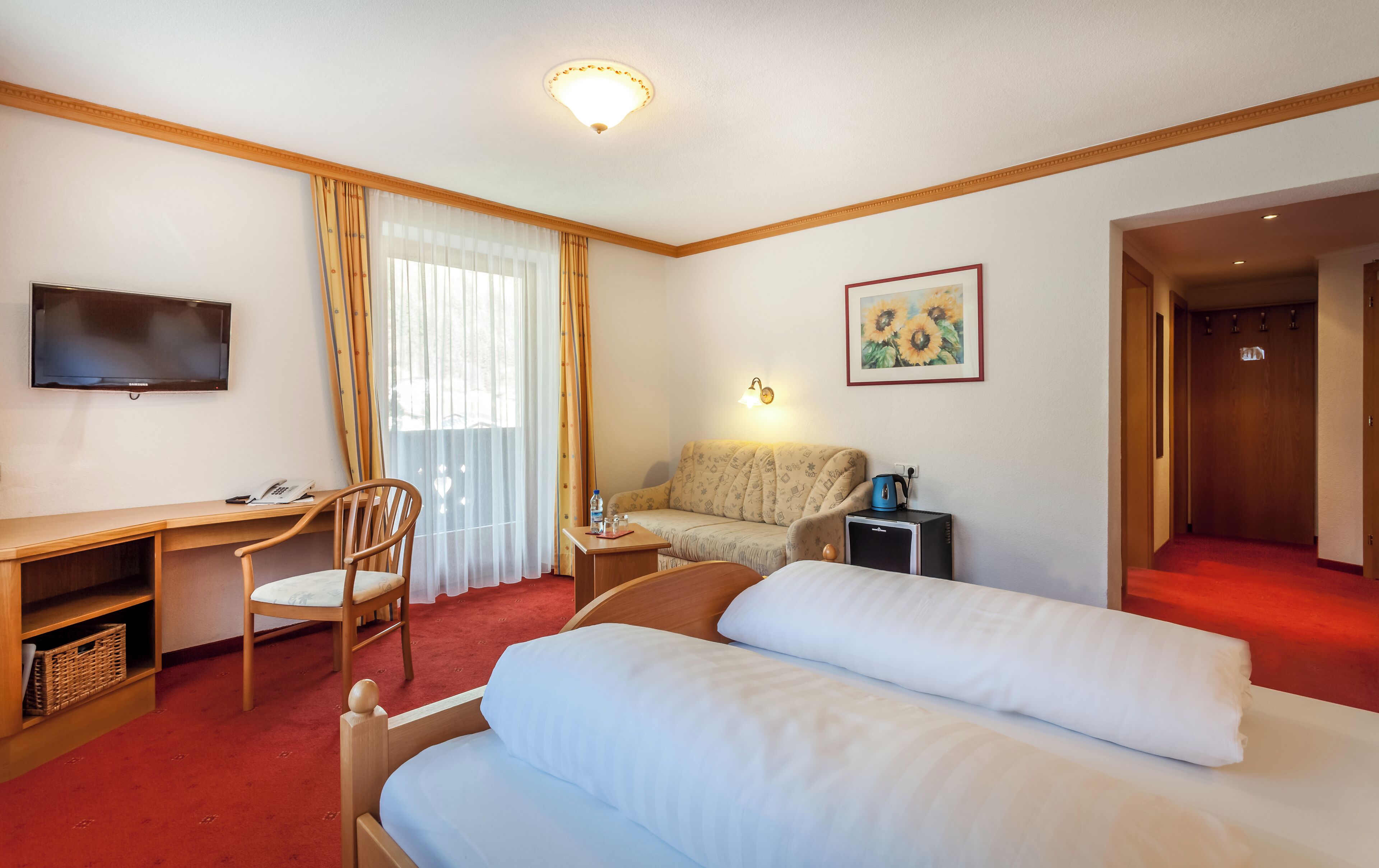 A hotel room with a bed, a desk, a chair, a television, a sofa, and a painting.