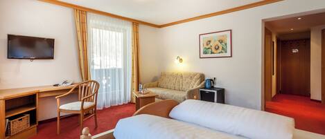 A hotel room with a bed, a desk, a chair, a television, a sofa, and a painting.