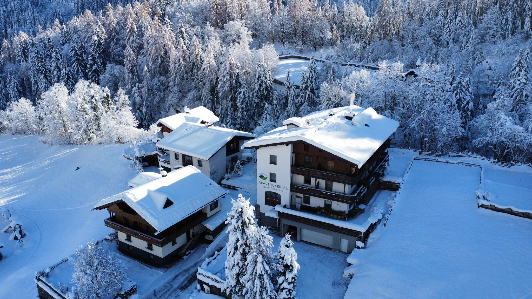 Uma pousada coberta de neve com vários edifícios, cercada por uma floresta.