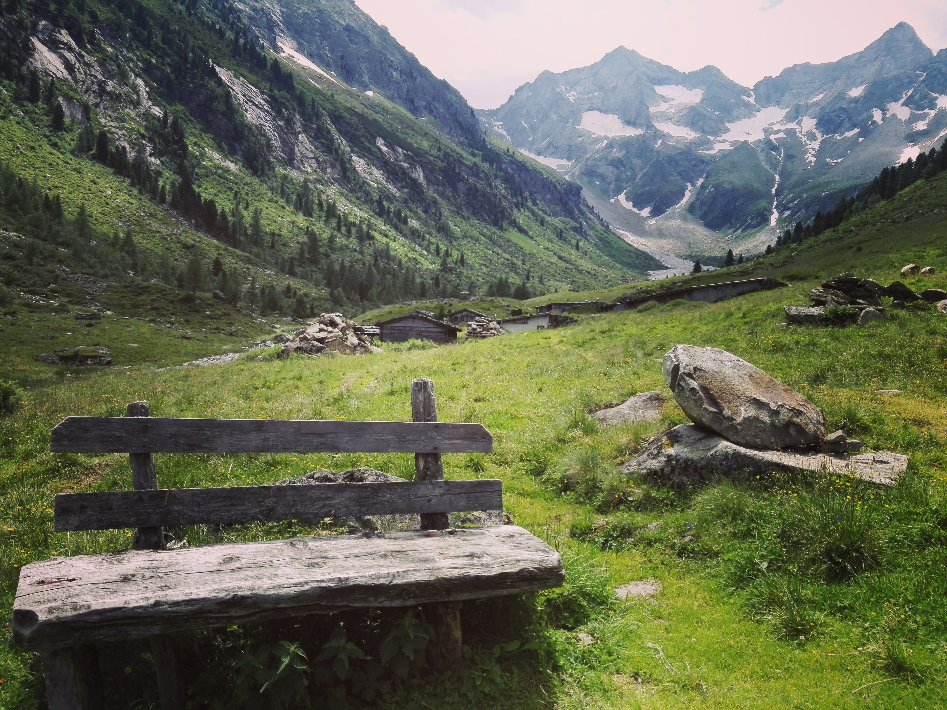 A wooden bench in a mountainous area with a view of a valley and distant mountains.