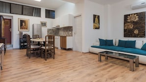 Un'ampia zona giorno con divano, tavolino e tavolo da pranzo. C'è un angolo cottura con pensili e frigorifero. La stanza ha un soffitto alto con lucernari e un quadro appeso al muro.