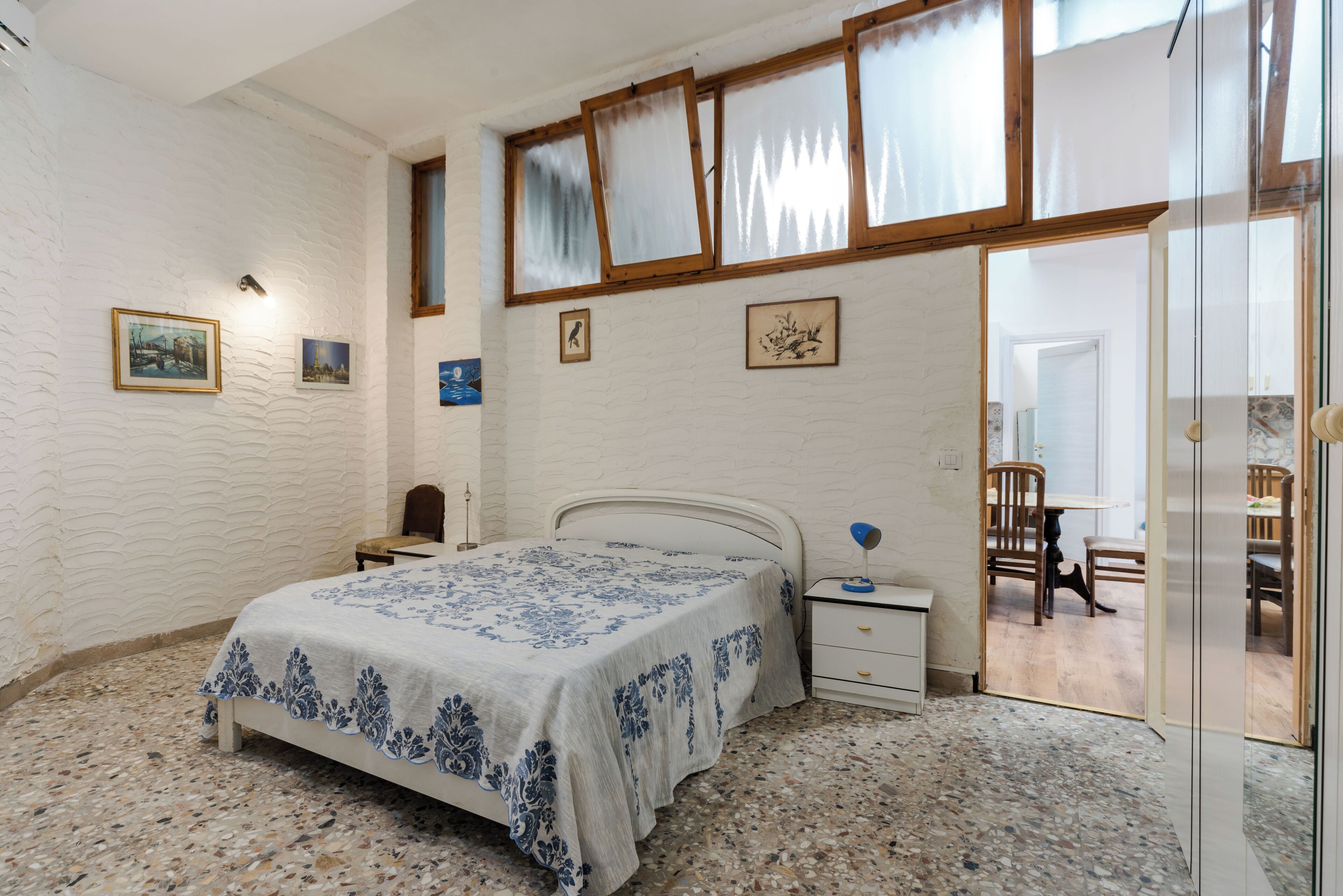 A bedroom with a bed, nightstands, a chair, a table, and a door leading to another room.