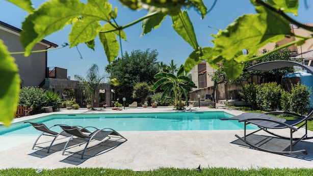 Una piscina con lettini, immersa nel verde e circondata da edifici.