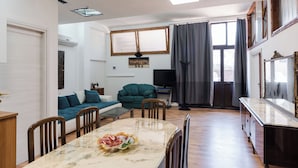 Un soggiorno con tavolo da pranzo, sedie, divano, televisore e una finestra con tende.