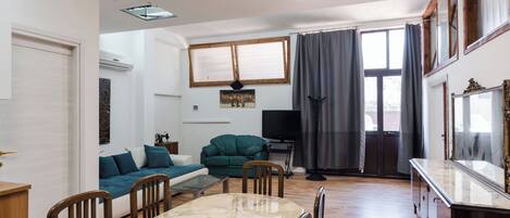 A living room with a dining table, chairs, a sofa, a television, and a window with curtains.
