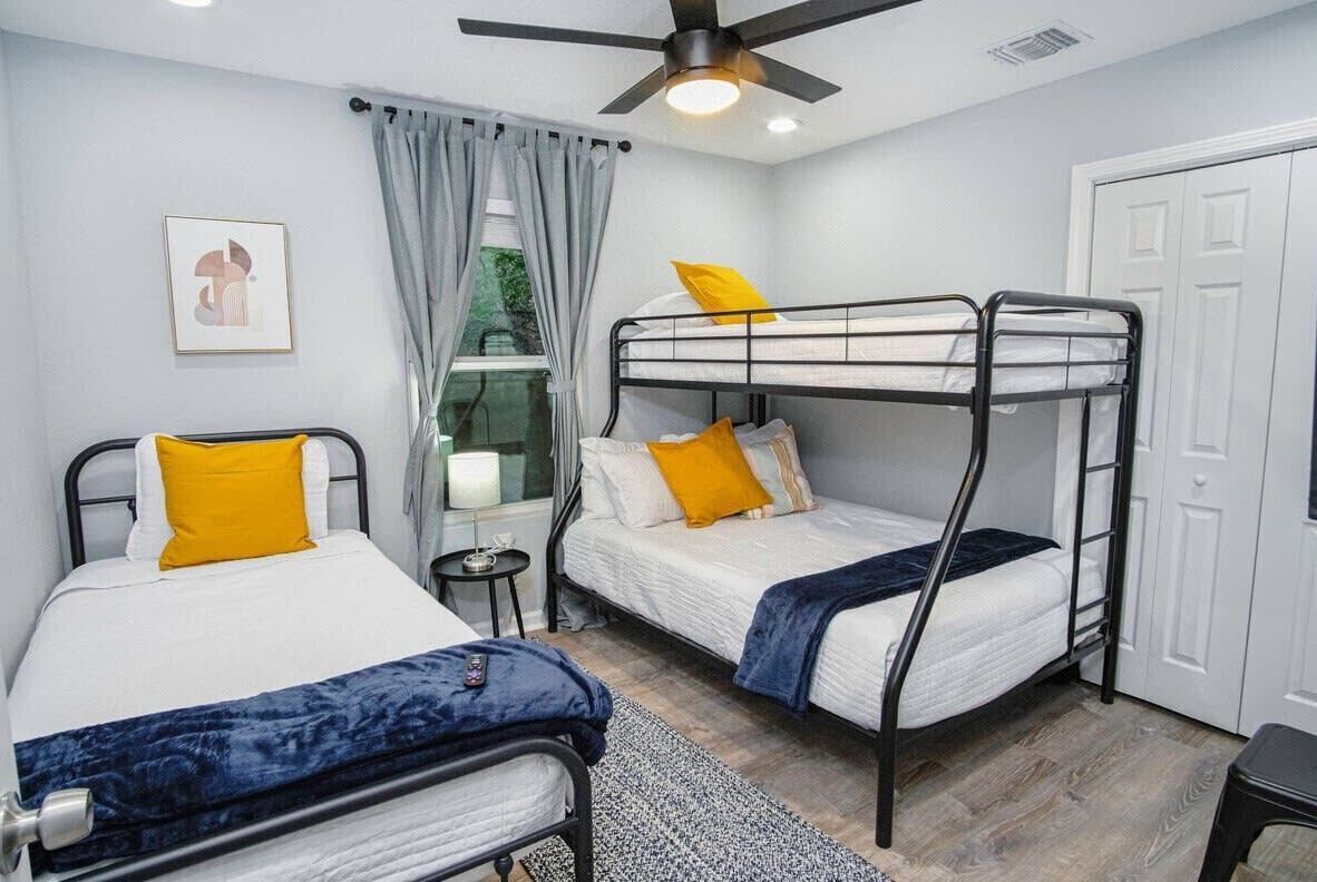 A room with bunk beds, a ceiling fan, a small table with a lamp, and a door.