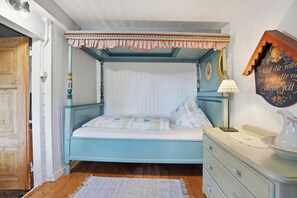 A bedroom with a four-poster bed, a bedside table, a lamp, and a dresser.