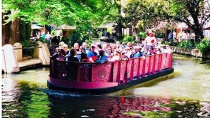 Een smalle boot met passagiers, omgeven door groen en een waterweg.