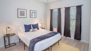 Een slaapkamer met een bed, twee nachtkastjes, een plafondventilator en een raam met gordijnen.