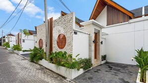 A modern residential street with houses featuring stone walls, wooden accents, and potted plants. - Oslen Villa by Kozystay - Canggu (Canggu)