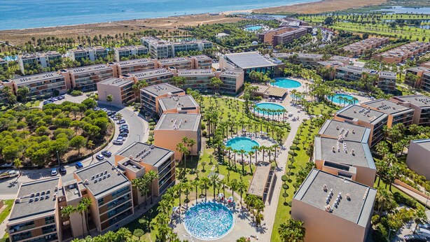 Un complexe hôtelier comprenant plusieurs bâtiments, un espace piscine central et une vue sur la plage.