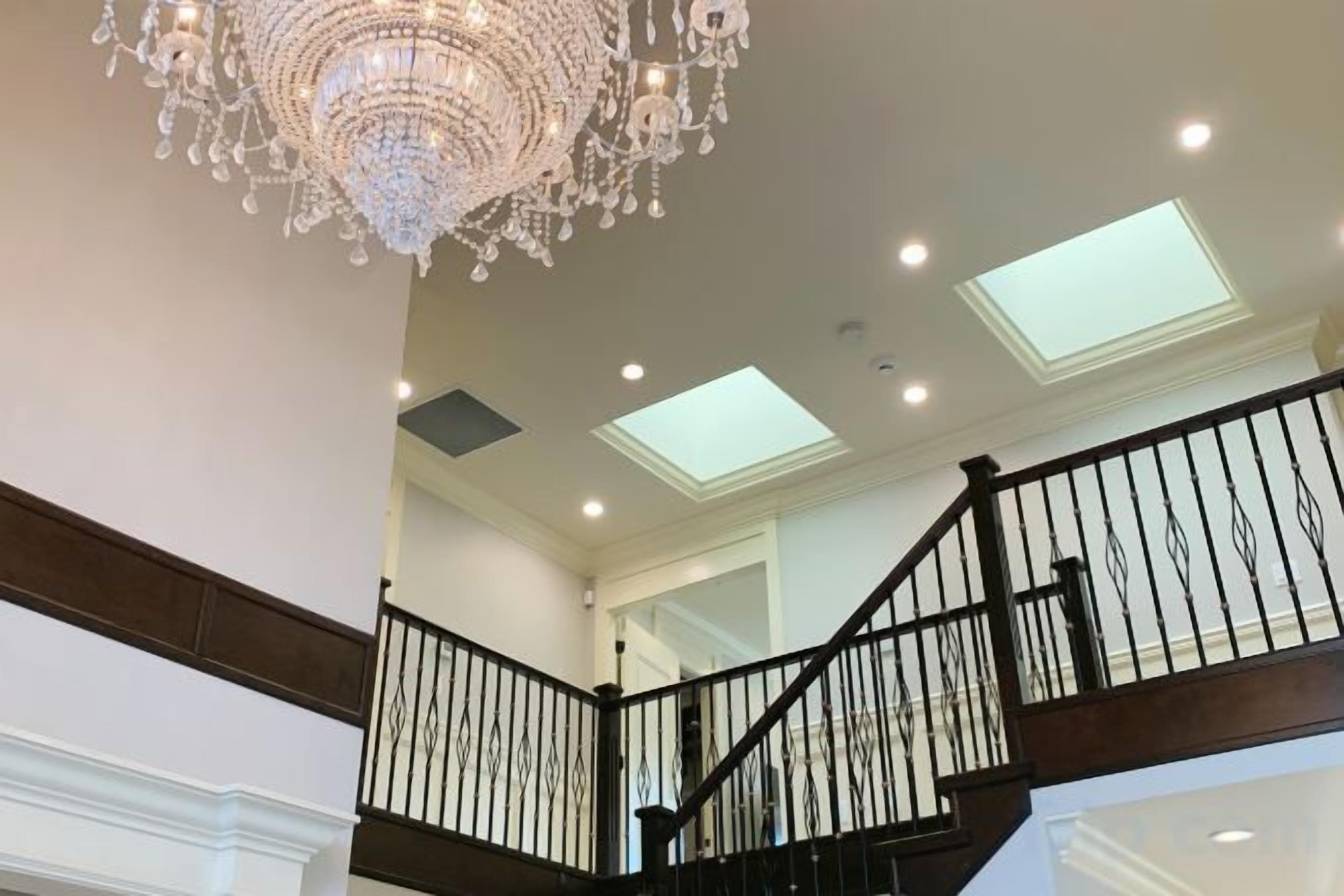 A grand staircase with a chandelier, skylights, and a black railing.