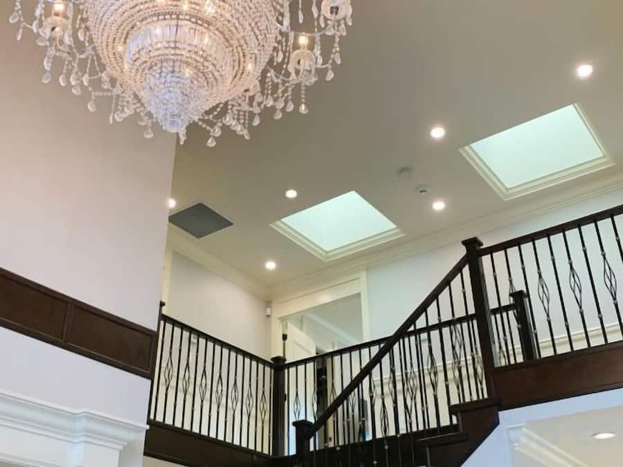 Eine prächtige Treppe mit einem Chandelier, Oberlichtern und einem schwarzen Geländer.