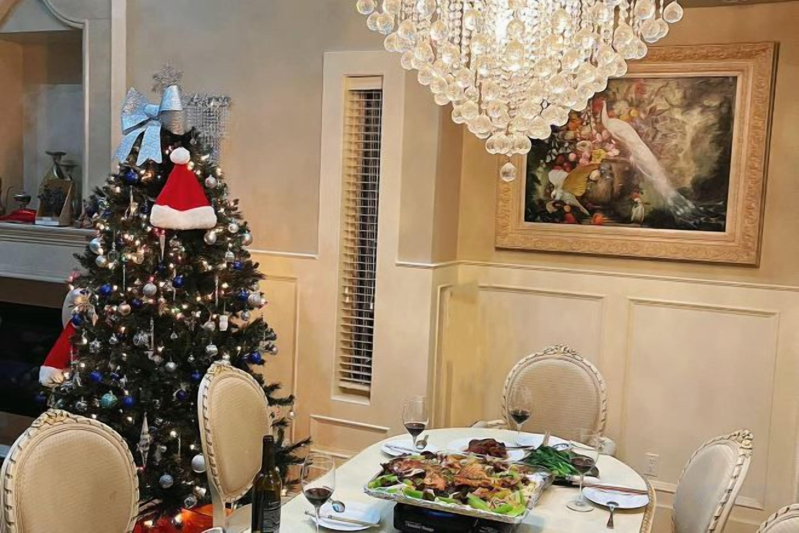 A dining area with a Christmas tree, a chandelier, and a painting on the wall.