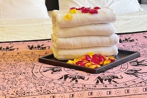 A stack of white towels on a tray with rose petals, placed on a patterned tablecloth. - Vancouver Love Home Luxury Inn (Richmond)