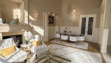 A spacious living room with a fireplace, a dining area with a chandelier, and a kitchen with white cabinets.