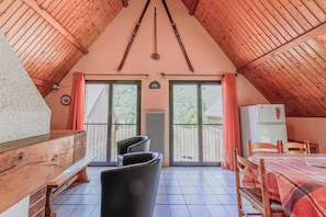 Une pièce chaleureuse avec un plafond en pente, un banc en bois, une table avec des chaises et une vue dégagée grâce à de grandes portes coulissantes.