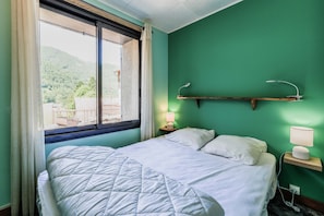 Une chambre à coucher avec un lit, une fenêtre avec des rideaux, une lampe de chevet et une table de chevet.