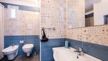 A bathroom with a bidet, toilet, and sink, featuring patterned tiles and a mirror.