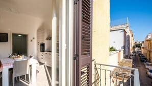A balcony with a table set for dining, a sliding glass door, and a view of a narrow street with parked cars. - Apartment 'Casa Vacanze Lu Rizzaru' with Private Terrace, Balcony & Air Conditioning (Nardò)