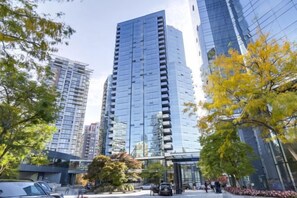 A modern high-rise building with a glass facade, surrounded by trees and other buildings. - Downtown Luxury Suite w/ Private Kitchen, Laundry, Parking (Vancouver)