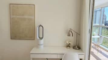 Ein modernes Hotelzimmer mit einem weißen Schreibtisch, einem großen abstrakten Gemälde, einem Fön, einer Lampe und Blick ins Freie.