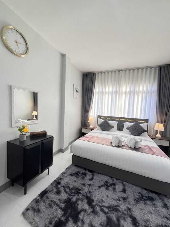 A modern bedroom with a large bed, a bedside table with a lamp, a wall clock, a mirror, and a decorative plant. - Ali House Patong (Patong)