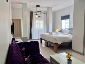 A hotel room with a bed, a desk with a computer, a purple sofa, and a small table with flowers. - Ali House Patong (Patong)