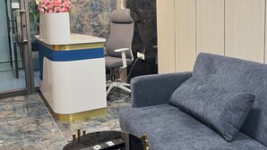 Un espace d’accueil moderne comprenant un comptoir de réception, un canapé gris et une petite table d’appoint.