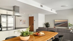 A modern kitchen with stainless steel appliances, a wooden dining table with a potted plant, and a grey sofa in the living area. - Gordon Beach Bright Stay by Sea N' Rent (Tel Aviv)