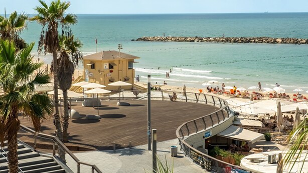A beachside promenade with a wooden deck, palm trees, and a building with a sign '7'. - Gordon Beach Bright Stay by Sea N' Rent (Tel Aviv)
