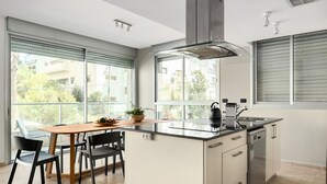 A modern kitchen with a central island, a dining area with chairs, and large windows offering a view of the outside. - Gordon Beach Bright Stay by Sea N' Rent (Tel Aviv)