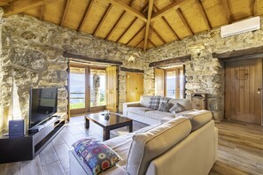 A stone-walled room with a wooden ceiling, a television, a sofa, and a coffee table.