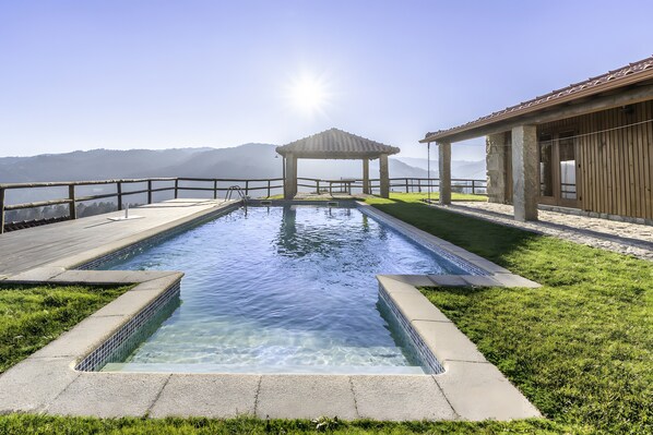 A rectangular swimming pool with clear water, surrounded by a wooden deck and a grassy area.