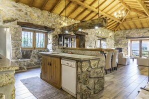 A rustic kitchen with stone walls, wooden beams, and a built-in dishwasher.