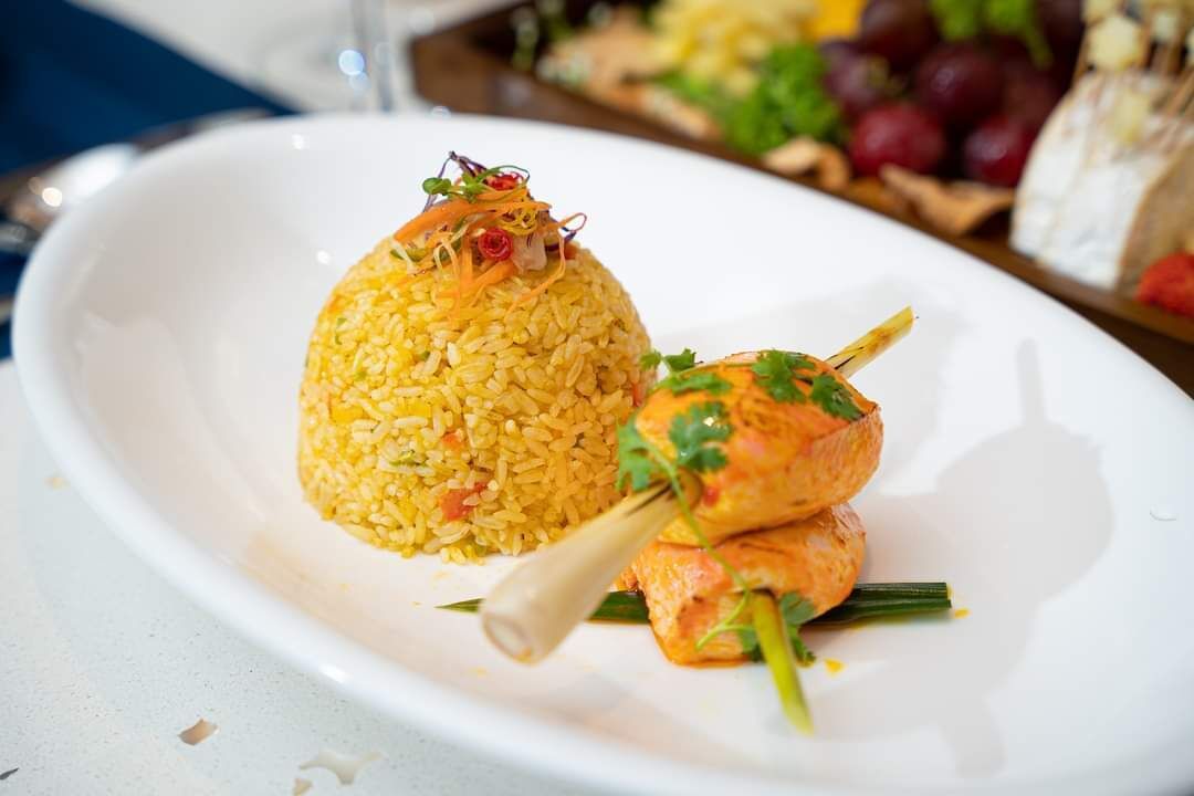 A plate with yellow rice and grilled chicken skewers.