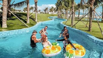 Piscina com água azul cristalina, cercada por palmeiras e uma área gramada.