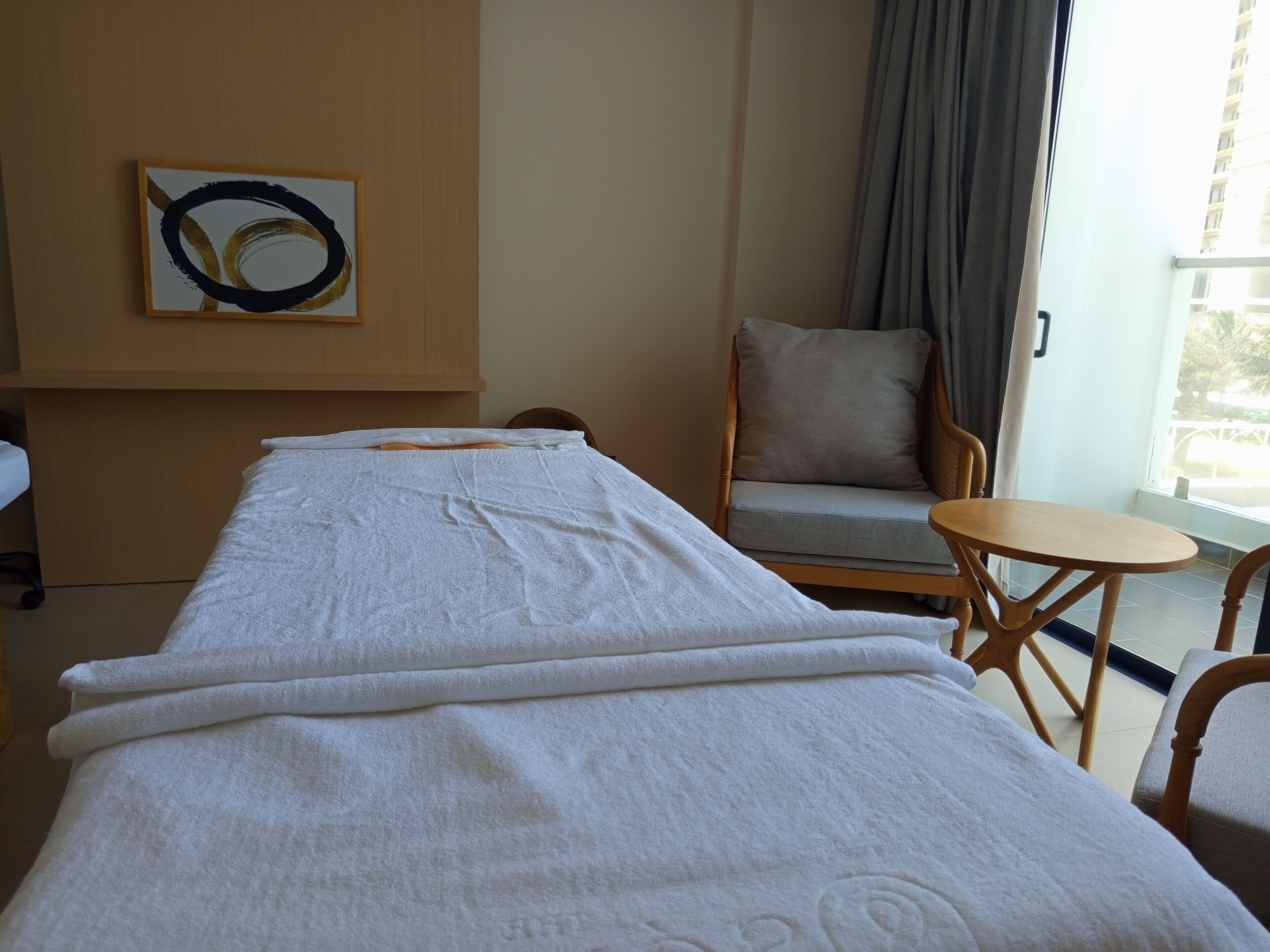 Une chambre d’hôtel équipée d’une table de massage, d’une chaise, d’une petite table ronde et d’un tableau au mur.