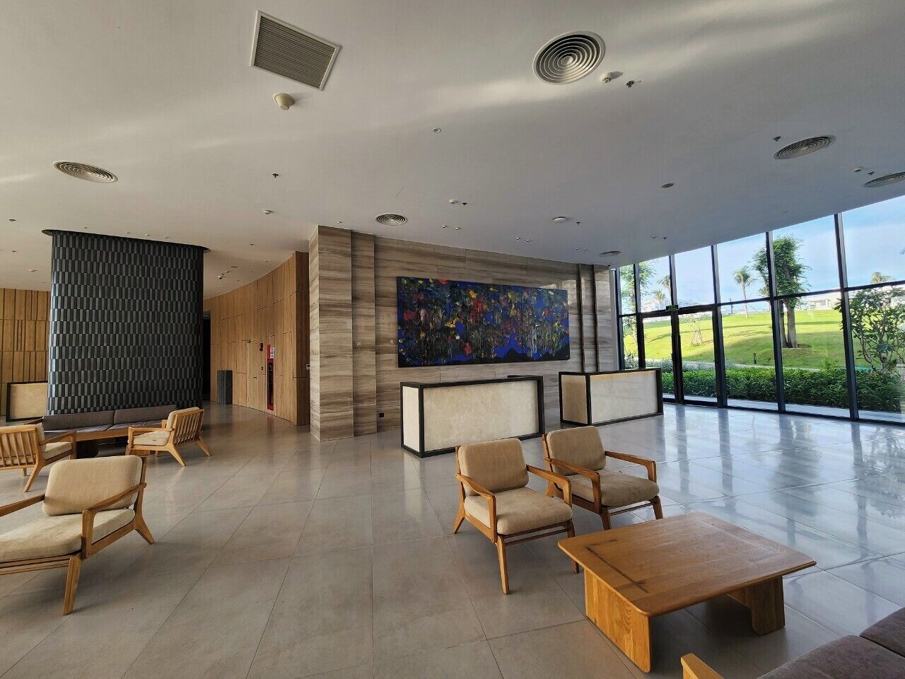 A spacious lobby with modern furniture, a large abstract painting, and large windows offering a view of the outdoors.
