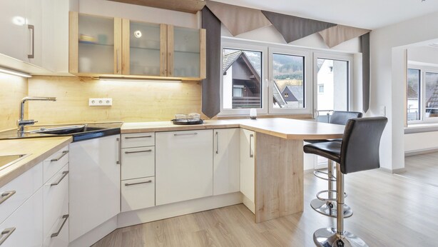 Une cuisine moderne avec des meubles blancs, un plan de travail en bois et un tabouret de bar.