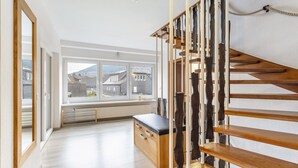Une pièce spacieuse avec un escalier en bois, un banc et une grande fenêtre donnant sur les bâtiments environnants.