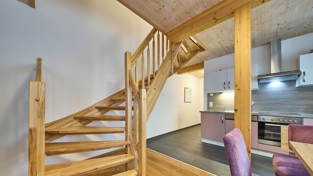 A wooden staircase leading to a kitchen area with modern appliances and a dining table. - Ferienwohnung Lisa (Bad Mitterndorf)
