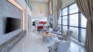 A spacious living room with a flat-screen TV, a round coffee table, and grey armchairs. A kitchen is visible in the background. - The Ascent Suites Genting Highlands (Genting Highlands)
