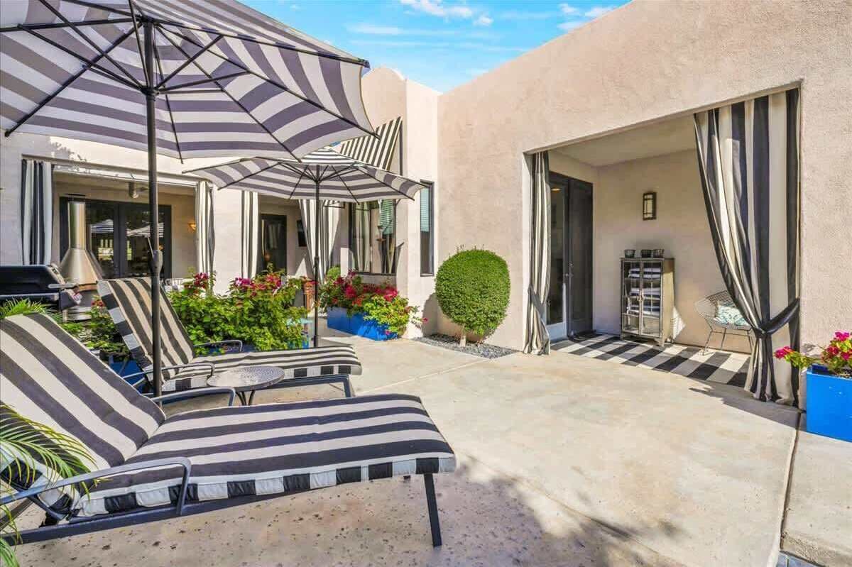 A patio with striped lounge chairs, a grill, and potted plants.
