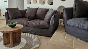 A modern living room with a sectional sofa, a round wooden coffee table, and a decorative wall with various objects.