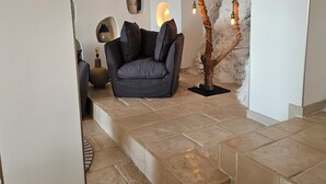 A modern living room with a stone-tiled floor, a dark grey sofa, and a unique tree sculpture with hanging lights.