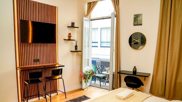 Een moderne hotelkamer met een bed, een televisie bevestigd aan een houten paneel, een balkon met een stoel en een kleine tafel.